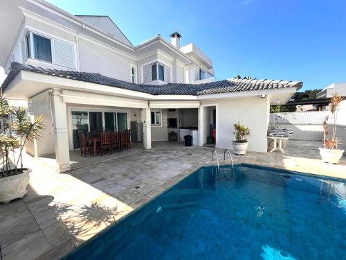 a villa with a swimming pool in front of a house at Casa Condomínio Fechado Hanga Roa Bertioga in Bertioga