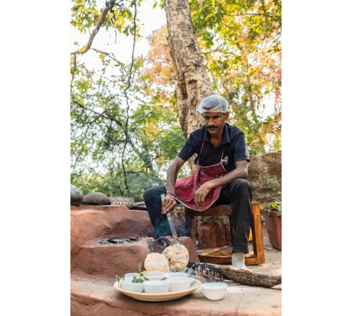 a man in an apron sitting on a table with food at Jungle Ghar in Pachmarhī
