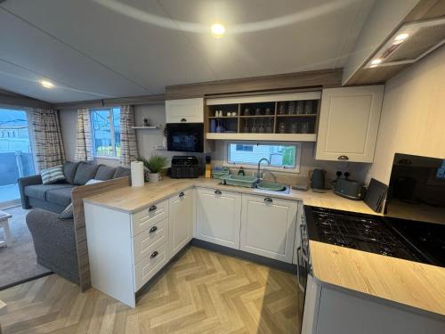 a kitchen with white cabinets and a living room at Fantasy Island - Eastgate F6 - The Ardennes with Hot Tub - Coastal Caravan Breaks in Ingoldmells