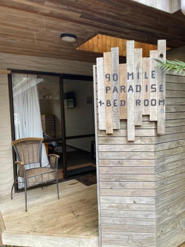 a porch with a chair and a sign on a wall at 90 Mile Paradise Ahipara in Ahipara