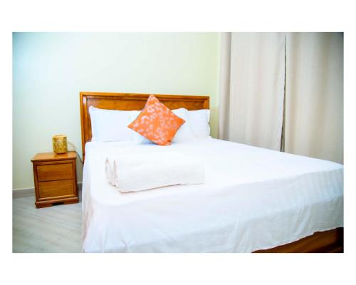 a bed with white sheets and an orange pillow on it at Cherryhomes at Mbezi Juu in Dar es Salaam