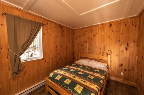 a bed in a wooden room with a window at Chalet des Boisés 10 in Murdochville