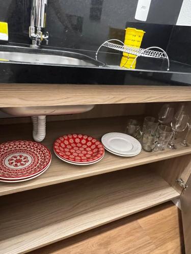 two red and white plates on a shelf under a sink at Guaja 745 - Apartamento Marie Lili in Belo Horizonte