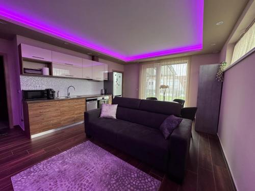 a living room with a couch and a kitchen with purple lights at Penthouse Happy Seasons in Hajdúszoboszló