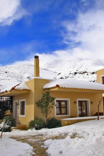 a yellow house with a snow covered mountain in the background at Earino in Kato Asites