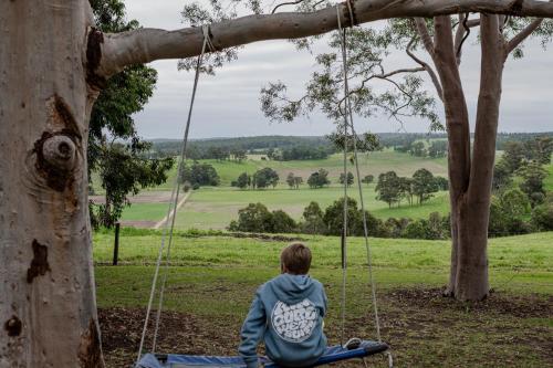 a boy sitting on a swing in a tree at Luxe HomeStay 2 BEDROOM Option at 6 O'Clock Shadows in Orbost