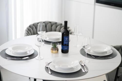 a white table with plates and glasses and a bottle of wine at Prestige Apartment Primošten in Primošten
