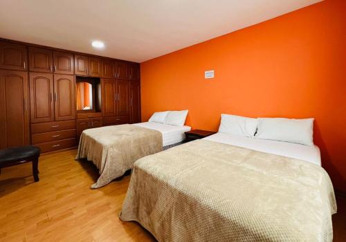 two beds in a room with an orange wall at 2 Cascada Apartment 2 Bedroom 2 Bath in Baños