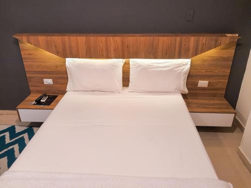 a bedroom with a large white bed with a wooden headboard at Gran Diamante Hotel Monteria in Montería