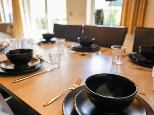 a wooden table with black bowls and plates and silverware at Mali in Gramsbergen