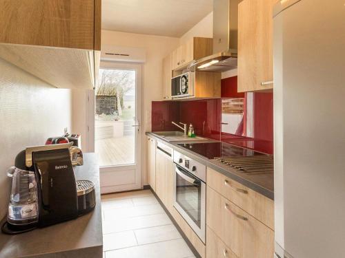 La cuisine est équipée de placards rouges et d'un four avec plaques de cuisson. dans l'établissement Maison rénovée avec jardin près du Canal de Nantes à Brest, idéale pour pêche et escapades nature - FR-1-306-870, à Blain