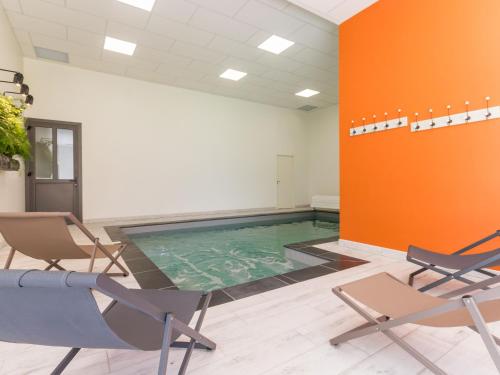 - une piscine dans une pièce avec des chaises et un mur orange dans l'établissement Élégant Gîte Rural avec Piscine Intérieure Chauffée près de Nantes - FR-1-306-913, à Châteauthébaud