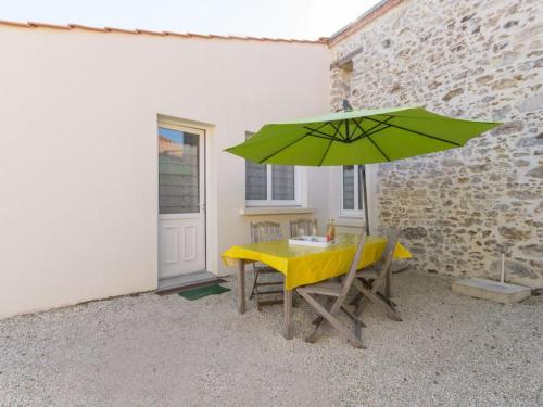 une table avec un parasol vert à côté d'un bâtiment dans l'établissement Gîte familial avec parc, jeux pour enfants et vélos, proche du Lac de Grand Lieu - FR-1-306-1040, à Touvois