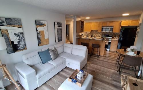 a living room with a white couch and a kitchen at Modern 1br Apt, Up to 4 people, Steps to 17th Ave, Downtown & Stampede in Calgary