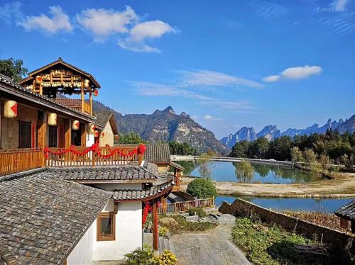 a house with a lake and mountains in the background at Dayong Antique Feature Resort in Zhangjiajie