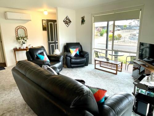 a living room with a leather couch and two chairs at Owl House on the Corner in Kingscote