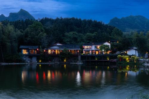 a house on the shore of a lake at night at Zhangjiajie Ldyllic Pondside Timber Lodge in Zhangjiajie