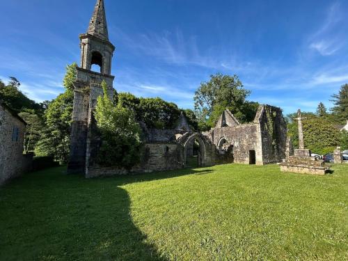 an old church with a tower and a grass field at Appartement dans un moulin avec terrasse in Plounéventer