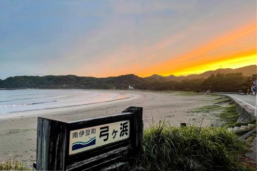 a sign on a beach with the sunset in the background at GLOCE 弓ヶ浜 Guest Room 南伊豆の弓ヶ浜近くのゲストルーム in Minamiizu