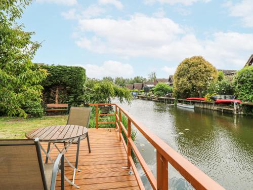 a wooden deck with a table and chair on a river at Kingfisher in Ely