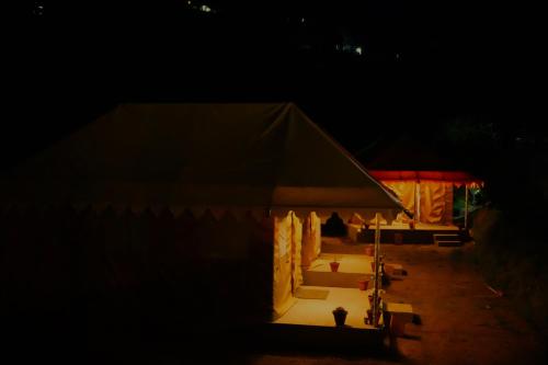 a tent with a table and chairs in the dark at Shakoon Camps & Farmstay Nainital in Nainital
