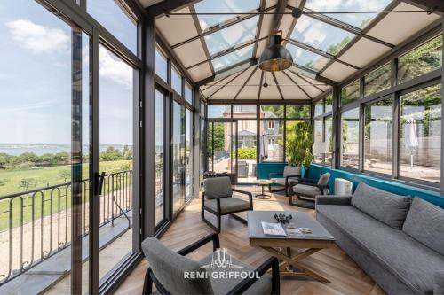 une véranda avec des fenêtres en verre, un canapé et des chaises dans l'établissement La Tour de l’Estuaire Sea View & Shared Garden 6 guests, à Honfleur