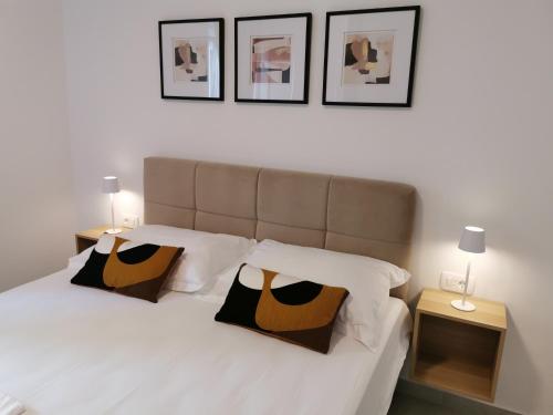 a bedroom with a white bed with three pictures on the wall at Apartment & Room Aleksandra in Rab