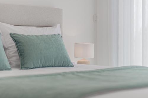 a white bed with a green pillow and a lamp at Caminho Real Guest Apartment I in Nazaré