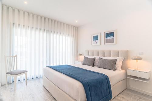 a white bedroom with a large bed and a chair at Caminho Real Guest Apartment I in Nazaré