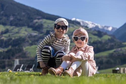 two people sitting on the grass with mountains in the background at Alpin Family Resort Seetal in Kaltenbach