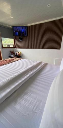 a white bed in a bedroom with a tv on the wall at De Pointé Resort & Resto in Campaka