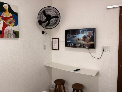 a bathroom with a tv on the wall and two stools at Pousada Cantinho de Minas Da Tânia in Cabo Frio