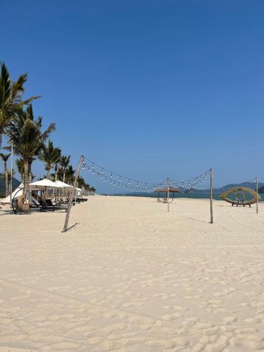 a sandy beach with a swing set and palm trees at Villa 4BR sát biển- Sonasea -Vân Đồn- Quảng Ninh in Thâm Câu
