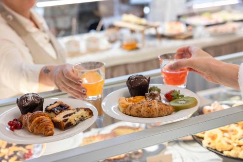 a woman holding two plates of food on a counter at Hotel Delle Terme Santa Agnese in Bagno di Romagna