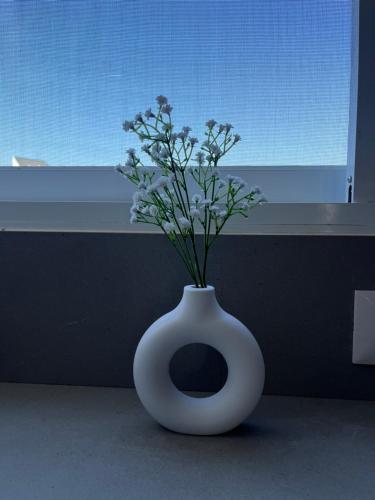 a white vase with flowers in it in front of a window at Boutique apartment in Rishon LeẔiyyon