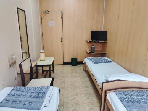 a room with two beds and a table and a tv at Milan Guest House in Mumbai