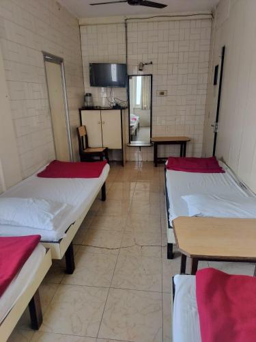 a room with three beds and tables in it at Milan Guest House in Mumbai