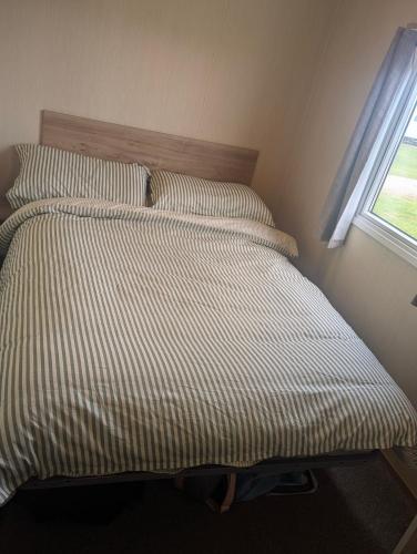 a bed with a striped comforter and two pillows at Abi Sunset - Camber Sands in Camber