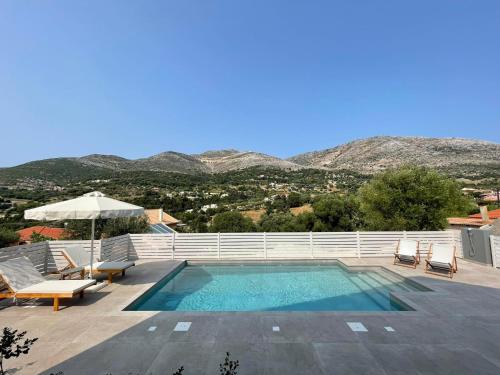 a swimming pool with chairs and an umbrella and mountains at Myrtia Villas I in Anomeriá