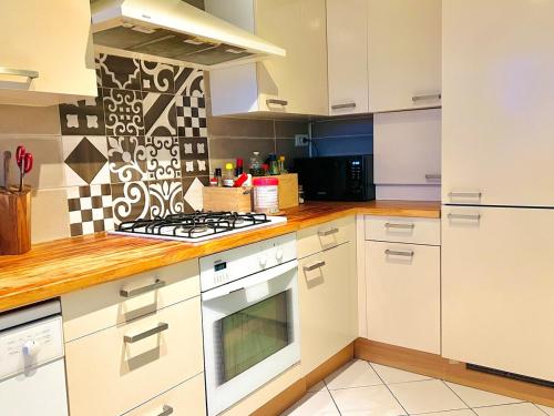 une cuisine avec des armoires blanches et un four à plaques de cuisson dans l'établissement Un Cocon Vert Canard à côté Paris 14ème - 3 pièce de 70m2 avec 2 chambres et un grand salon lumineux, à Montrouge