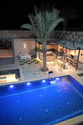 ein Swimmingpool bei Nacht mit einer Palme und einem Restaurant in der Unterkunft Lumen villa in Umm Uthainah