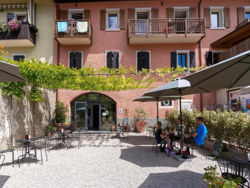 two people sitting at tables under umbrellas in front of a building at Apartment in Mezzolago with Lake Ledro Views in Mezzolago