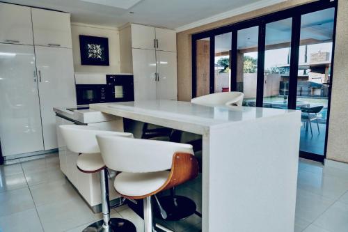 a kitchen with a white island with white stools at Escapade Lux Guesthouse in Gaborone
