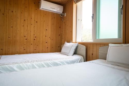 two beds in a room with wooden walls and a window at 오대산 달빛펜션 Odaesan Moonlight Pension in Pyeongchang 