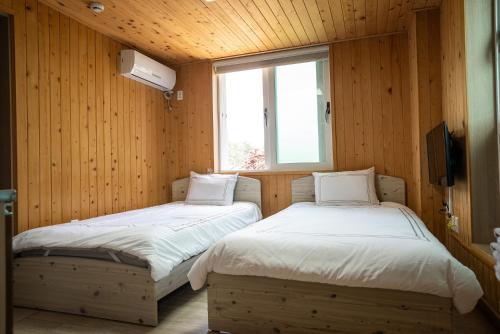two beds in a room with wooden walls and a window at 오대산 달빛펜션 Odaesan Moonlight Pension in Pyeongchang 