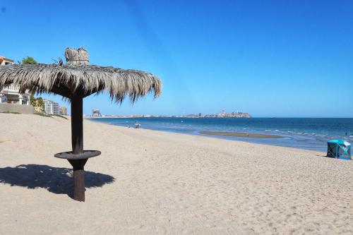 a straw umbrella on a beach with the ocean at Beachfront Condo on Sandy Beach, Las Palmas Resort, 24hrs Security, Free Parking, Free Wi-Fi in Puerto Peñasco