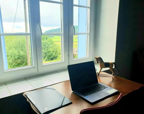 un ordinateur portable assis sur une table en bois devant une fenêtre dans l'établissement Maison de campagne, à Corancy