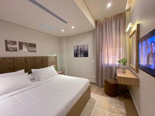 a bedroom with a white bed and a flat screen tv at شقة فاخرة 3 غرف نوم و حديقة خاصة في الشيخ زايد - Zayed Suites A in Sheikh Zayed