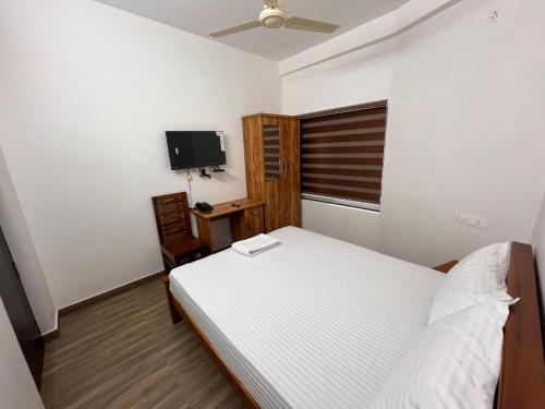 a bedroom with a bed and a desk and a tv at Ashtapadi Inn in Guruvāyūr