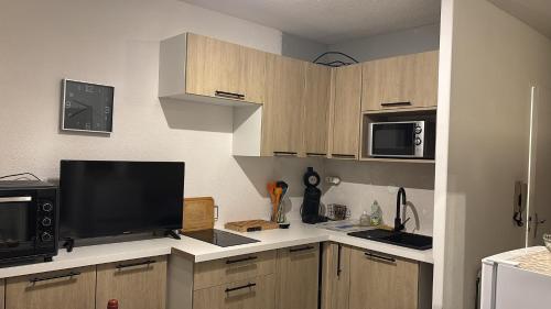 Il comprend une cuisine avec des placards en bois et une télévision à écran plat. dans l'établissement Studio jardin RDC 900 m des Thermes!, à Cazaubon